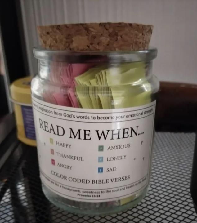 Jar with cork lid containing color-coded Bible verses on a textured surface.